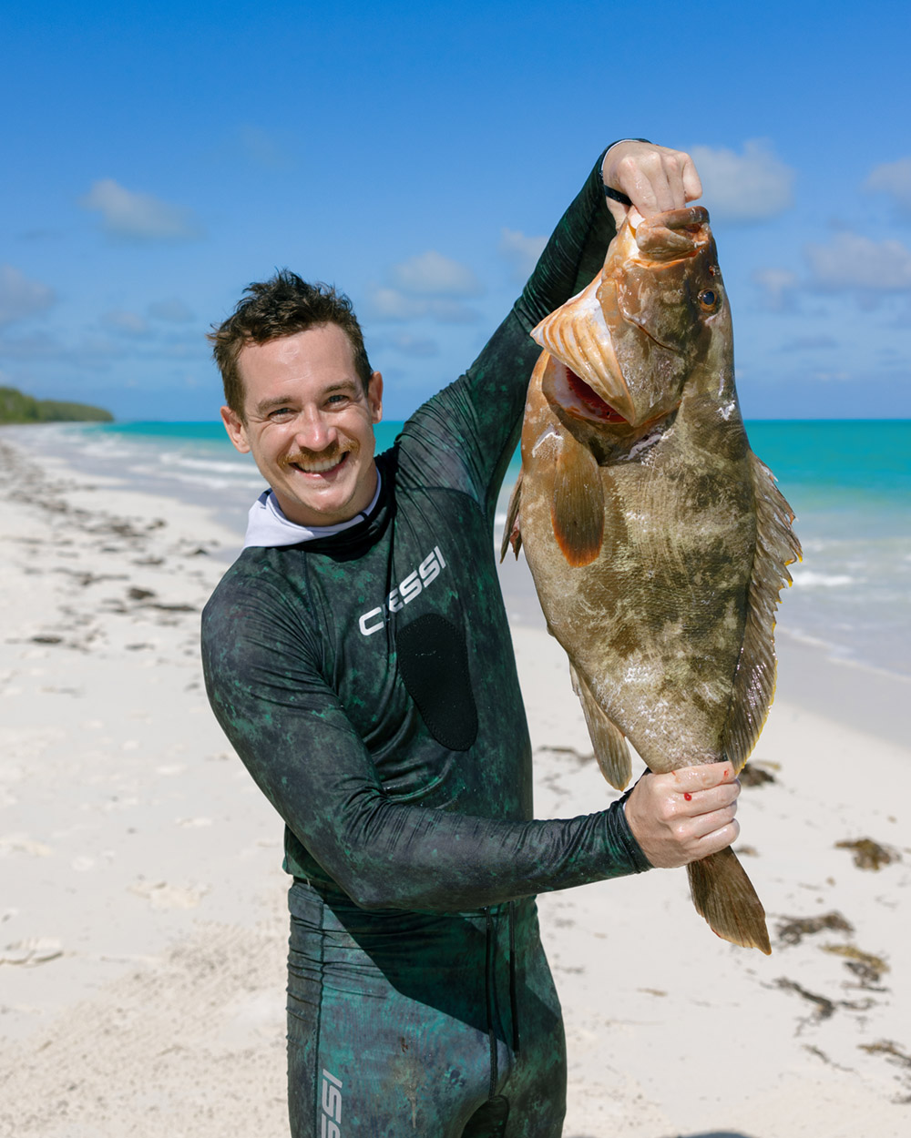 A man smiling and holding up his catch after chartering a spearfishing excursion