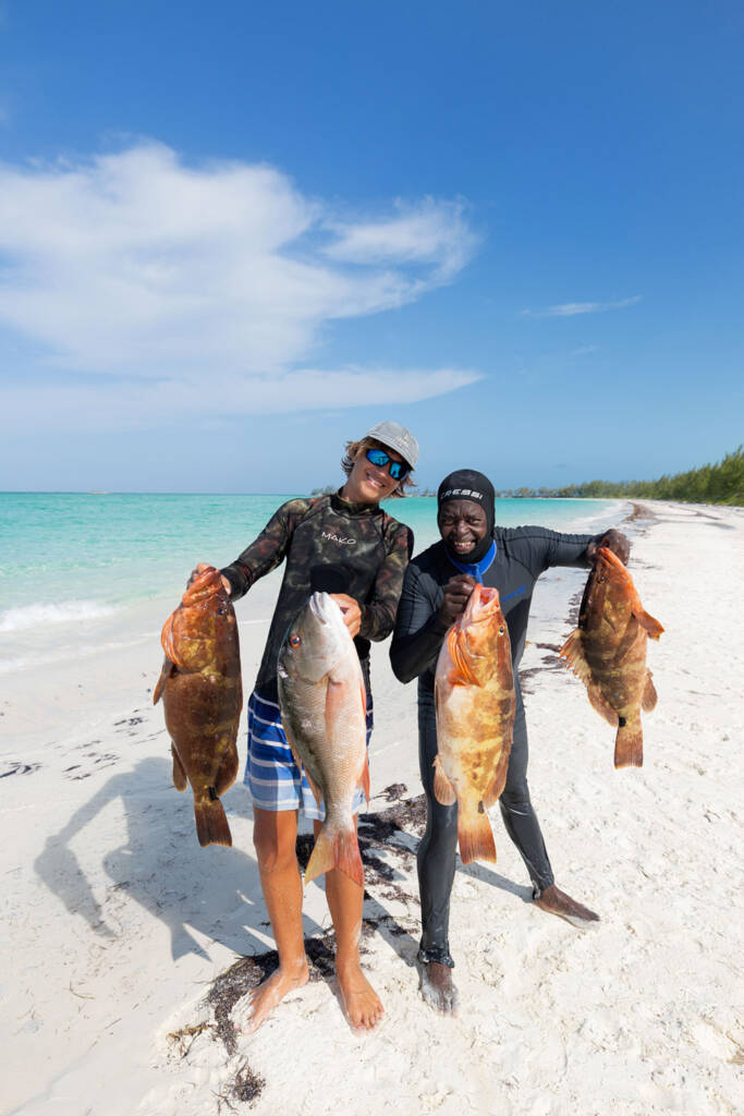 Two men on a beach holding up their catches from spearfishing in Andros Island